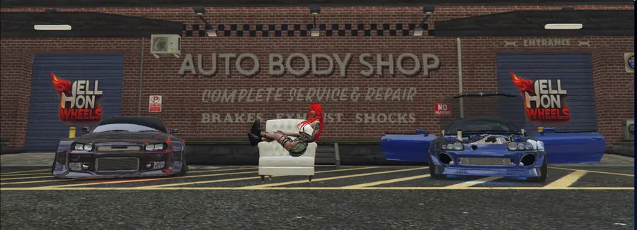 A body shop with two modified cars and a crew member lounging in an armchair between them